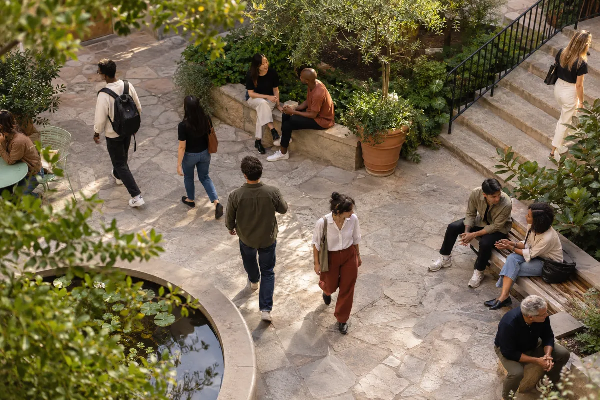 People walk and converse in a leafy public courtyard.