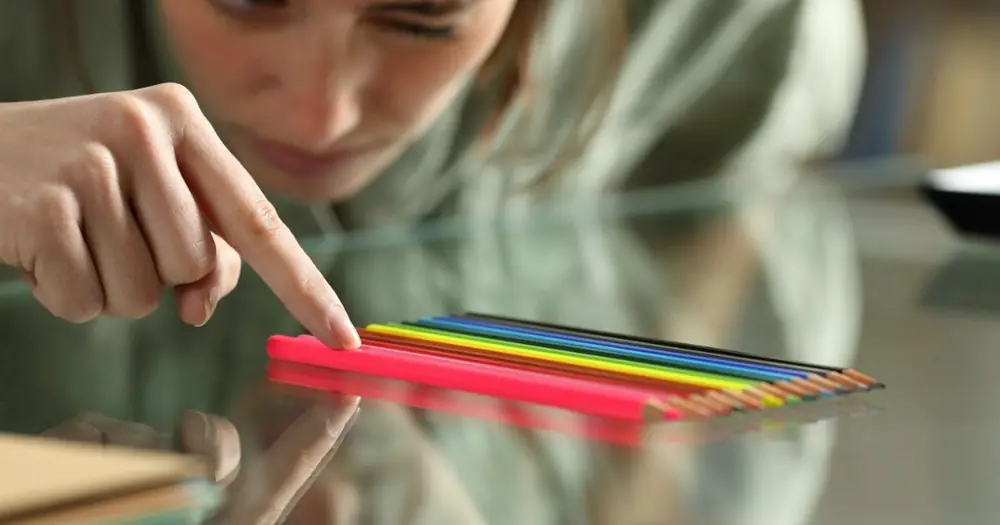 A child arranges colored pencils at a table.