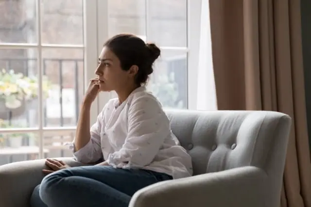 A woman sits thoughtfully beside a window.