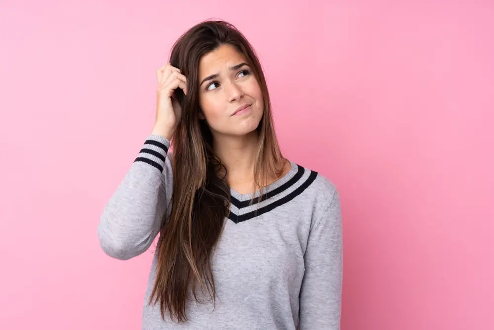 A woman pauses thoughtfully against a plain pink background.