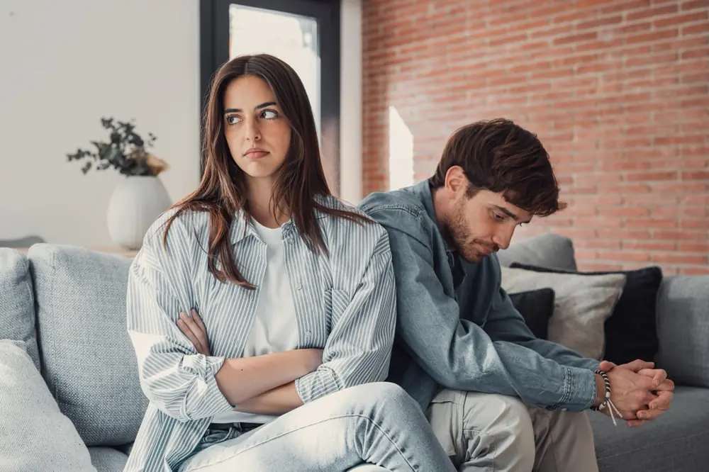 A couple sits apart on a sofa.