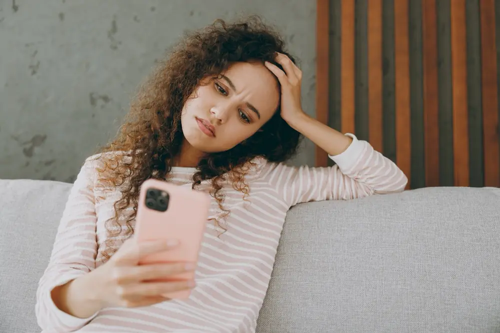 A woman sits on a sofa holding a phone.