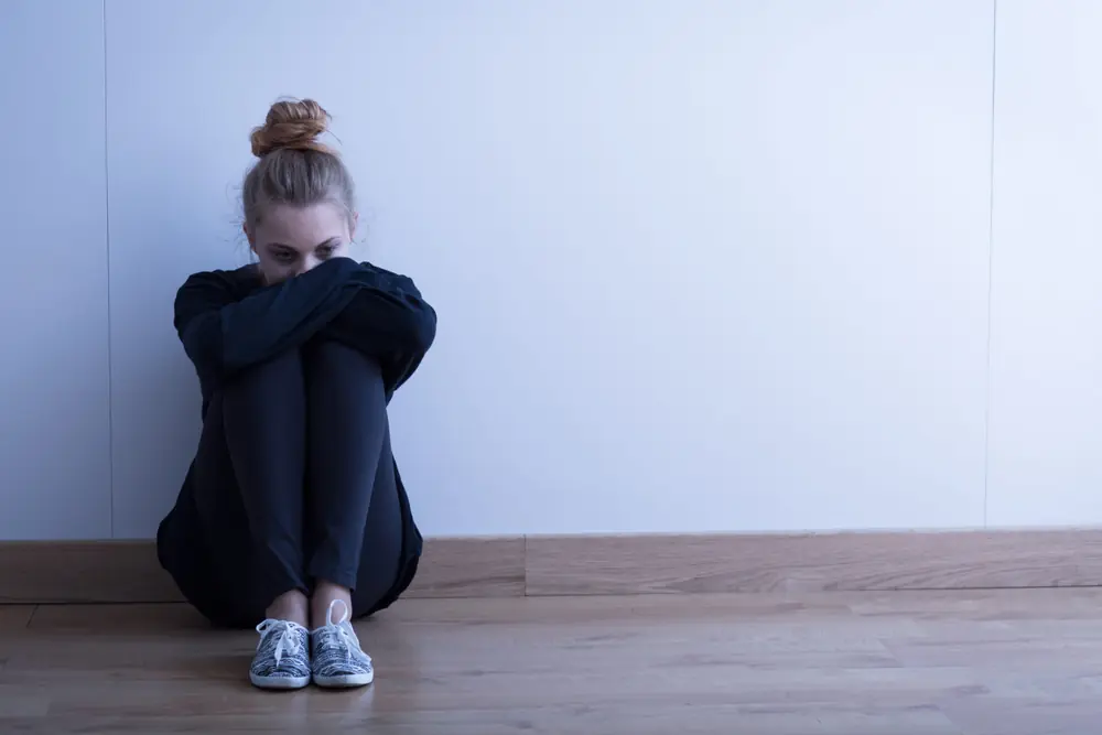 A person sits on the floor beside a pale wall.