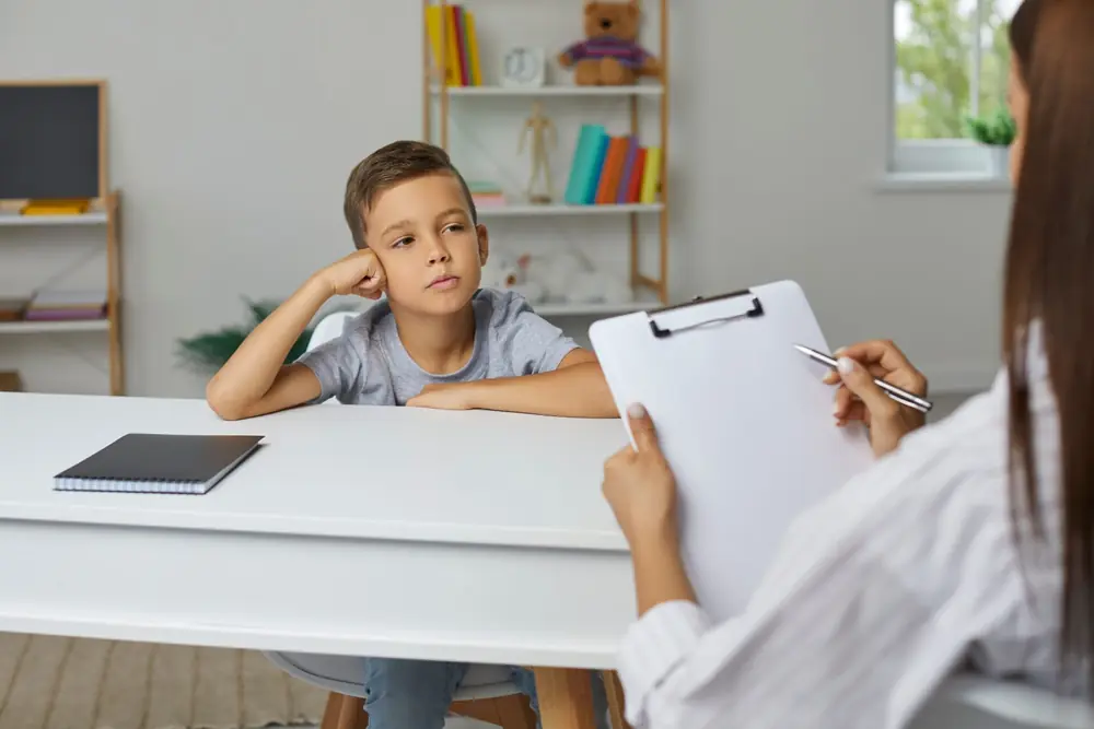 A young person sits across from an adult holding a clipboard.