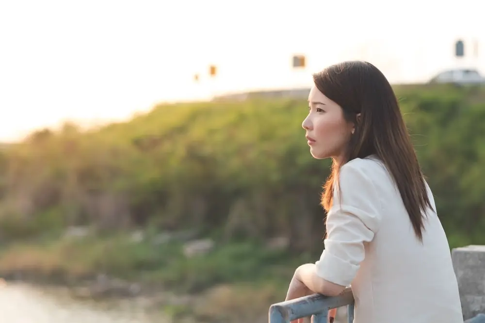A woman stands outdoors near sunlit grasses.