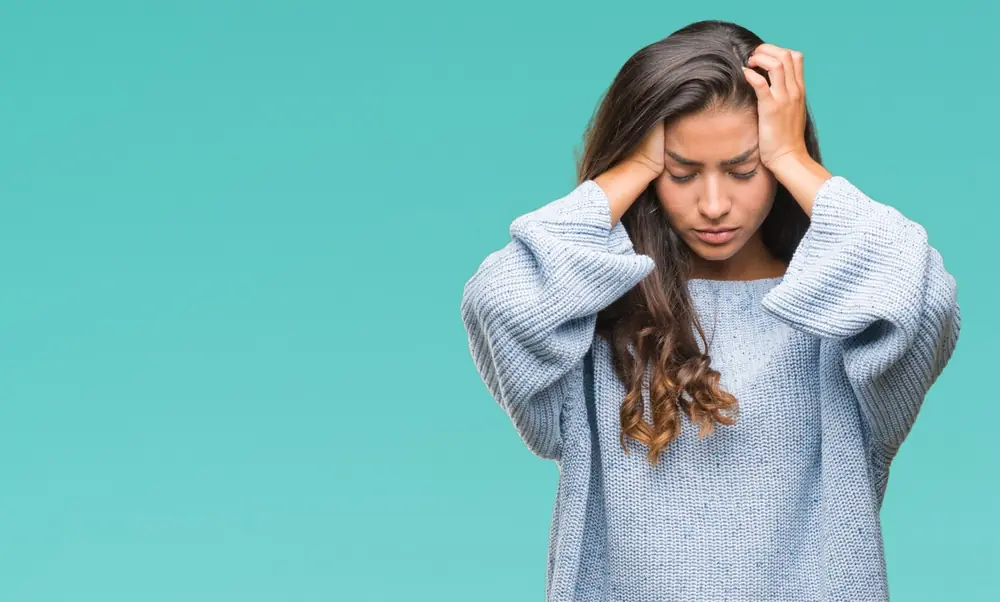 A woman holds her hands beside her head against a blue background.