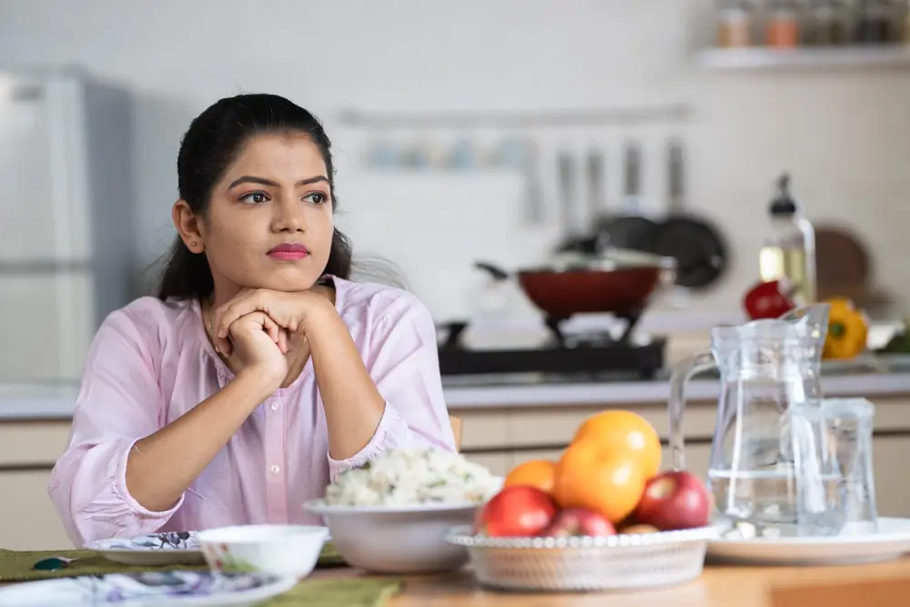 A woman sits at a table with food in front of her.