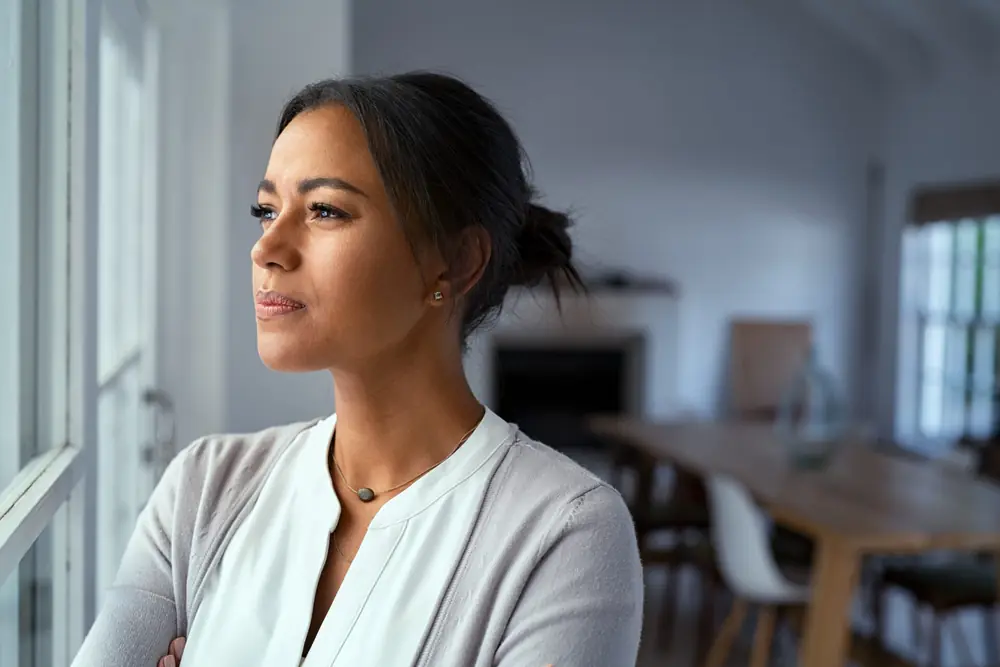 A woman looks through a window in soft daylight.