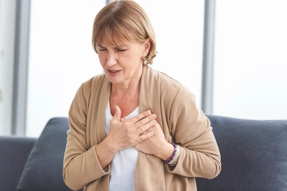 An older woman holds her hand against her chest.