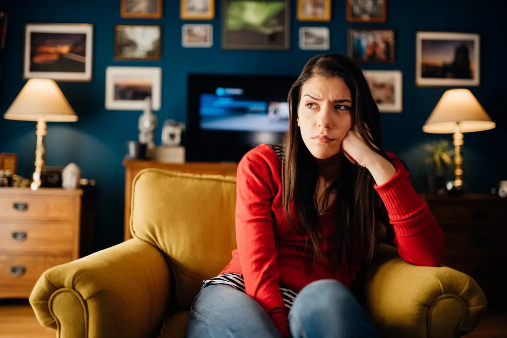 A woman sits on a sofa in a warmly lit room.