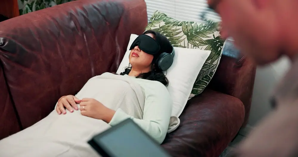 A person reclines on a sofa beneath a blanket.